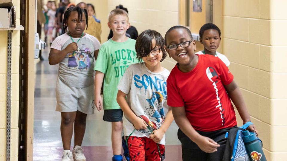 Smiling students in red, white, green shirts line up as a group to go to lunch