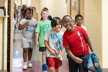 Smiling students in red, white, green shirts line up as a group to go to lunch