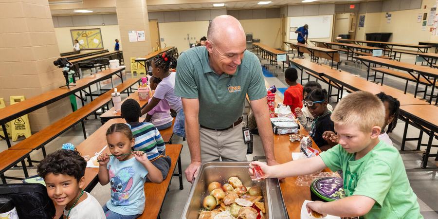 Math coach Dan St Onge wears a gray shirt and stands over a metal compost bin with students around him putting items in