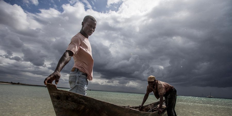Two men push a boat ashore in Mozambique with dramatic clouds in the background