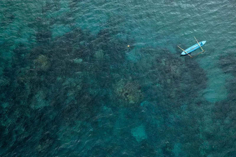 Aerial view of a small wooden boat with shallow coral reefs off the coast of Tamjung Karang, Buru Island, Maluku, Indonesia