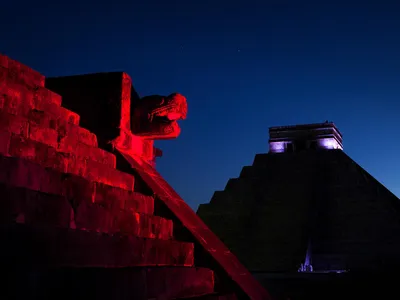 The pyramids of Chichen Itza shine red and shadowed against a dark blue sky