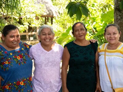 Four women, all memebers of the Las Vecinas beekeeping collective smile and pose together outside