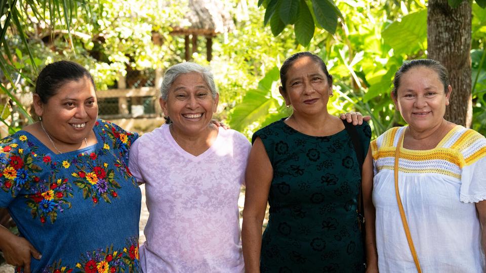 Four women, all memebers of the Las Vecinas beekeeping collective smile and pose together outside