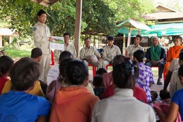 Preah Rumkel, Stung Treng, and Dorn Bann wear tan uniforms and stand and sit in front of a crowd during a meeting with fishers and community members in Cambodia