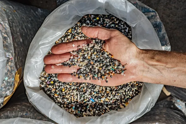 A hand holds hundreds of tiny plastic beads called nurdles, which are the raw material of plastic packaging and biobeads are used in sewage treatment to break down human waste
