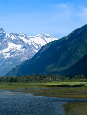 A river with snow covered mountains in the background on a sunny day