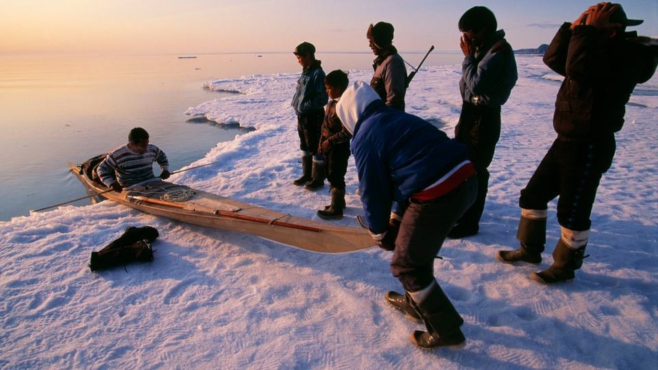 Inuit students standing on the ice, learning about building and operating traditional kayak