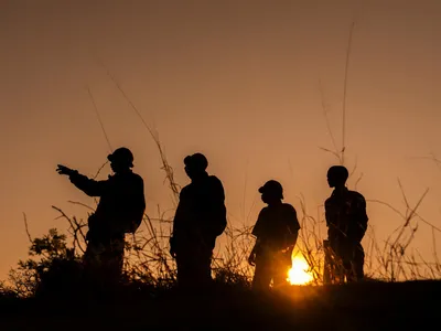Four rangers stand in silhouette against an orange sky in the Nyae Nyae Conservancy, Namibia