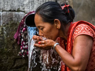 A women uses cupped hands to take a drink of water in Nepal