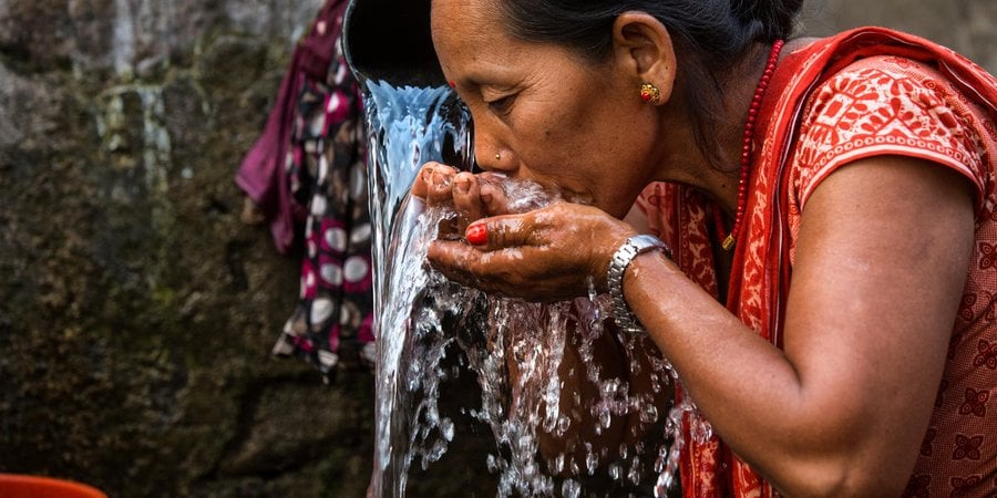 A women uses cupped hands to take a drink of water in Nepal