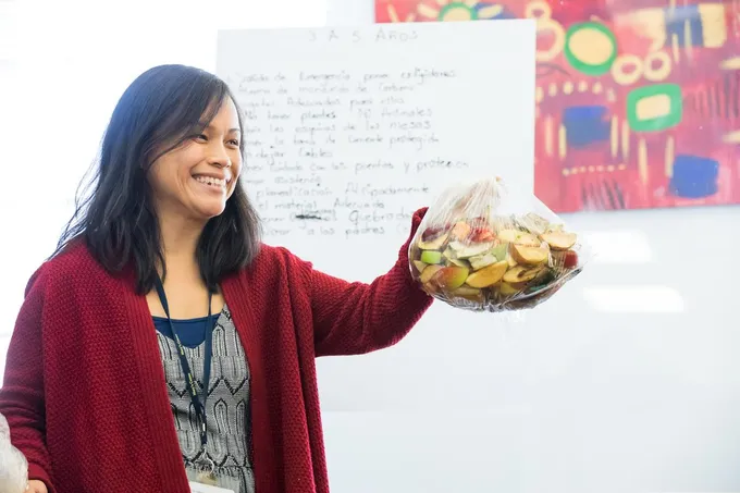 A woman wearing a red cardigan and blue shirt wiht brown hair holds out a bowl of food