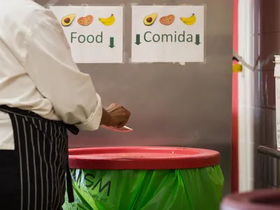 A chef puts food scraps into a trash can labeled "food / comida"