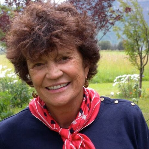 A headshot of a smiling older woman in front of a meadow