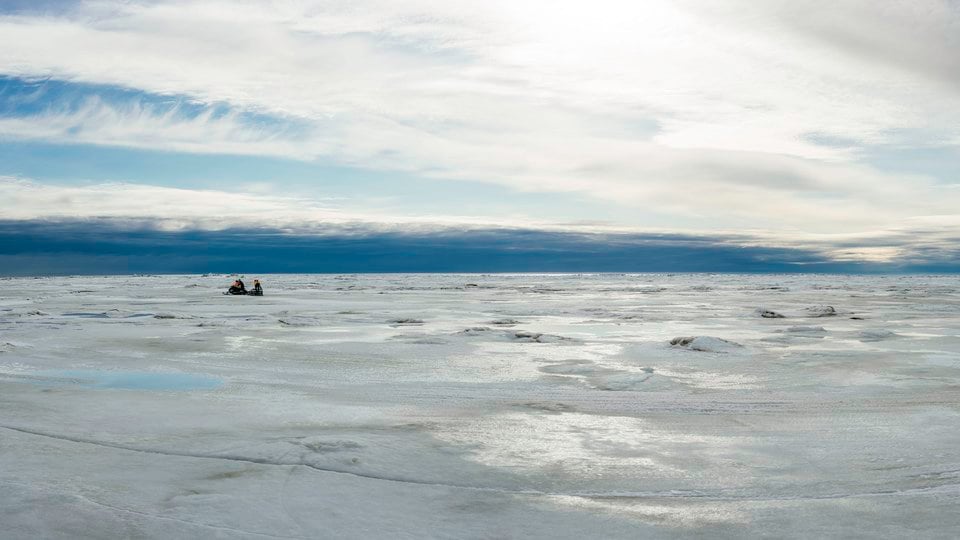 A snowmachine pulls a sled across sea ice near Wales, Alaska.