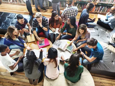 Group of college aged students sitting on around a table, in circle, looking at school materials