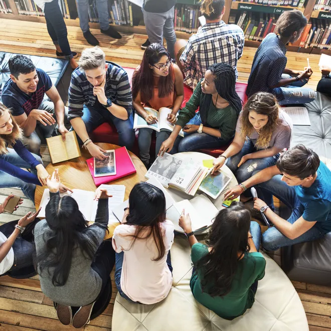 Group of college aged students sitting on around a table, in circle, looking at school materials