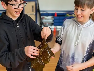 One student holds a piece of seaweed while another student looks at it with a smile