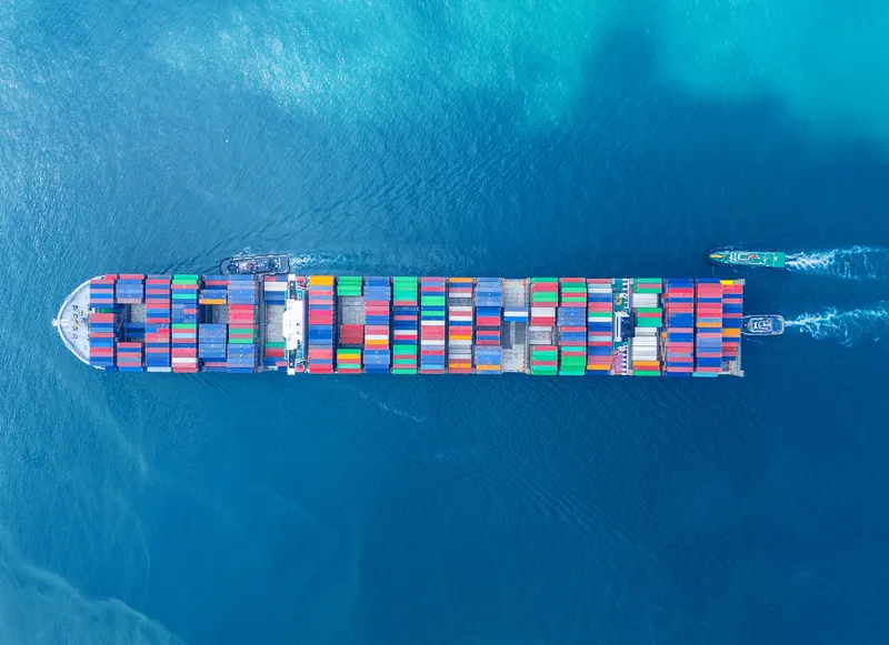 Aerial view looking down at a cargo vessel ship carrying hundreds of containers across the open ocean