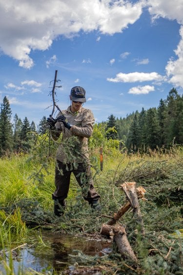 A Rio Grande Return crew member stands above a newly built artifical beaver dam