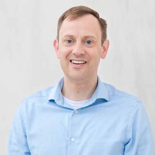 Seth Larson, wearing a light blue shirt, smiles against a white background