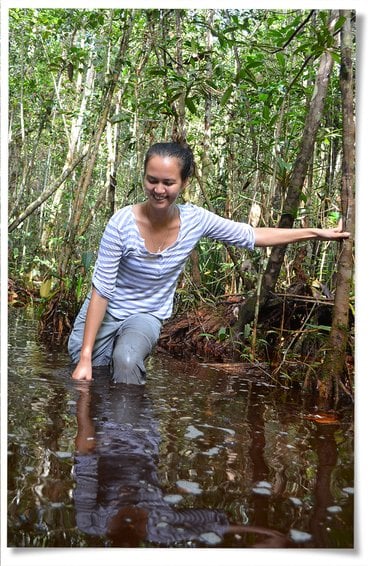 Stephanie Roe stands in wetland, leaning on tree