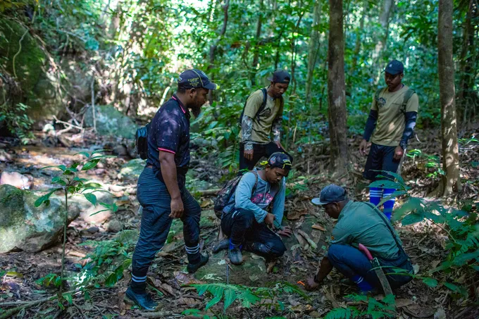 Uniformed men confer in a circle in the forest