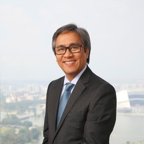 Headshot of a man with gray hair wearing a gray suit and glasses. His hands are clasped in front of him.