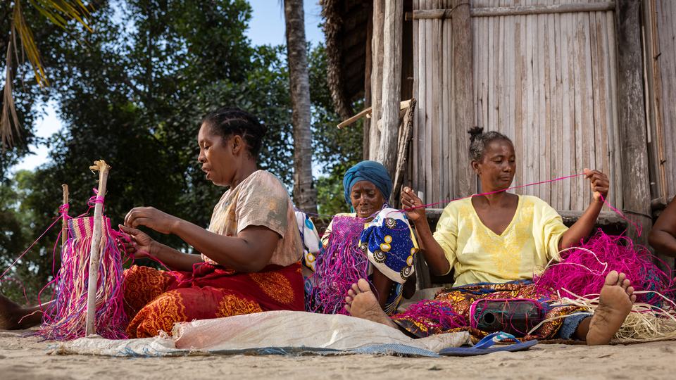 Women sitting on the ground measuring colorful yarn