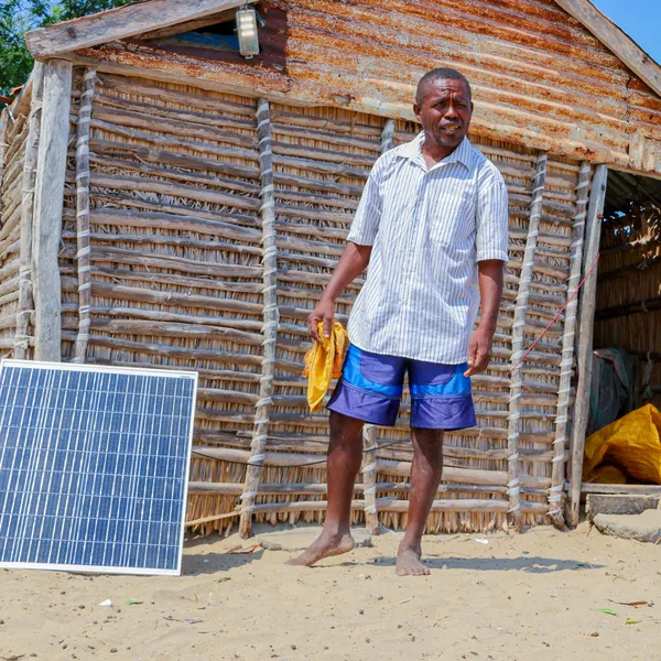 A person stands in front of his cabin next to a solar panel
