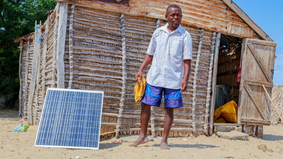 A person stands in front of his cabin next to a solar panel