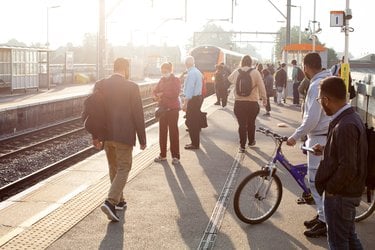 People stand on a public transportation platform one of whom has a bike as a train approaches
