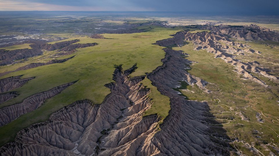 Aerial view of the south unit of Badlands National Park showing tall gray cliffs with green crass at the tip