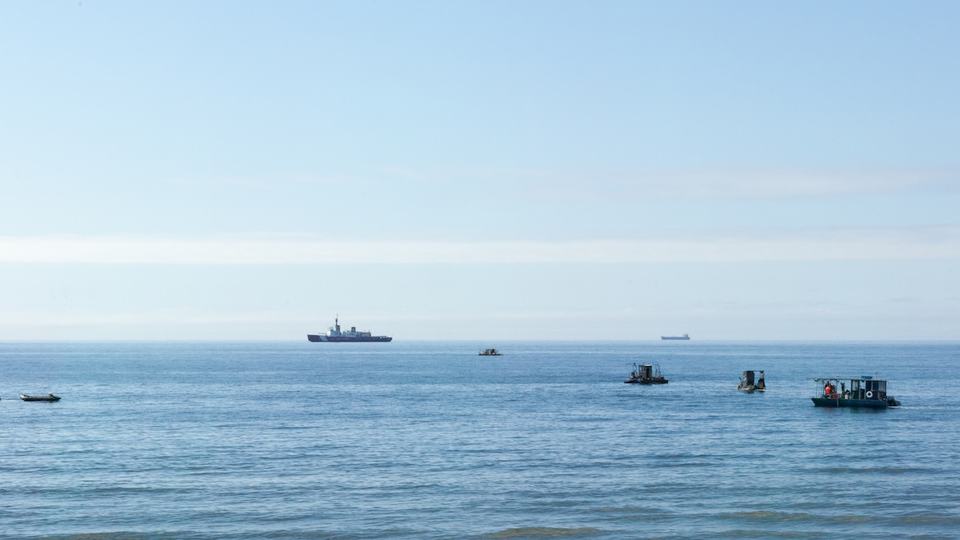A zoomed-out view of big and small boats on a wide open blue water