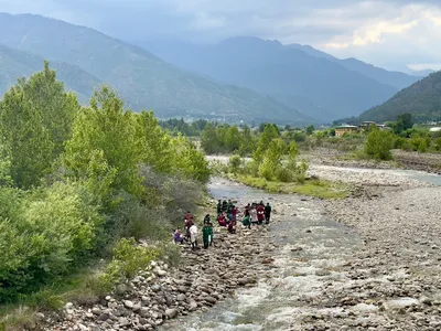 People stand on a riverbed with mountains in the background