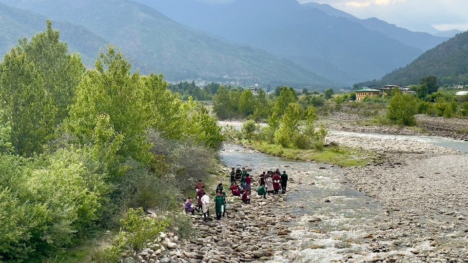 People stand on a riverbed with mountains in the background