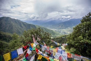 Colorful prayer flags in Bhutan are seen with a green landscape in the background.