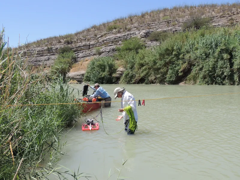 Three researchers stand in the Rio Grande stretching a rope across the water to collect eDNA samples and measure the environmental flow of the river.