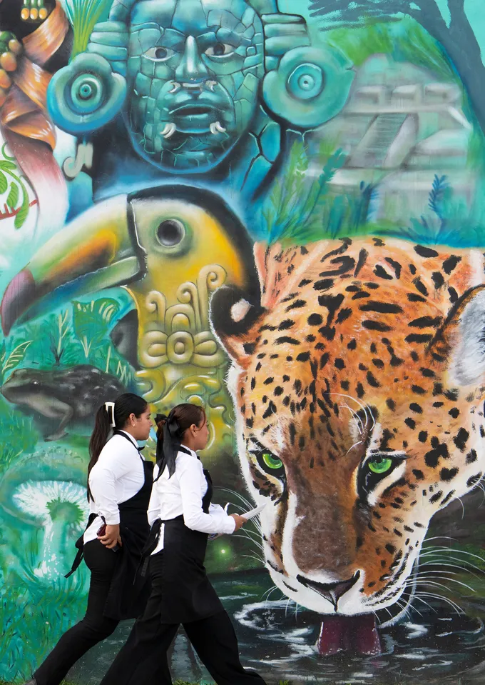 Two girls walk by a colorful mural of a jaguar and toucan