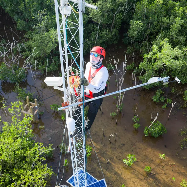 Aerial photo of a man in a helmet and mask on a white radio tower, checking equipment