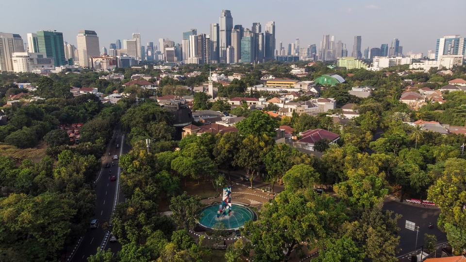 Trees amid a street in the foreground, with tall buildings in a city skyline in the background