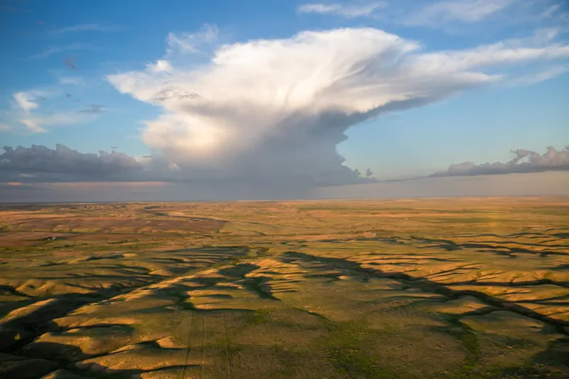 Grasslands in the foreground with a large white cloud against blue skies.