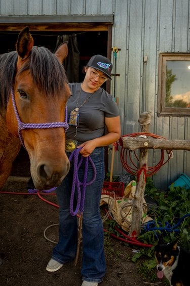 A woman stands outside a barn with a horse
