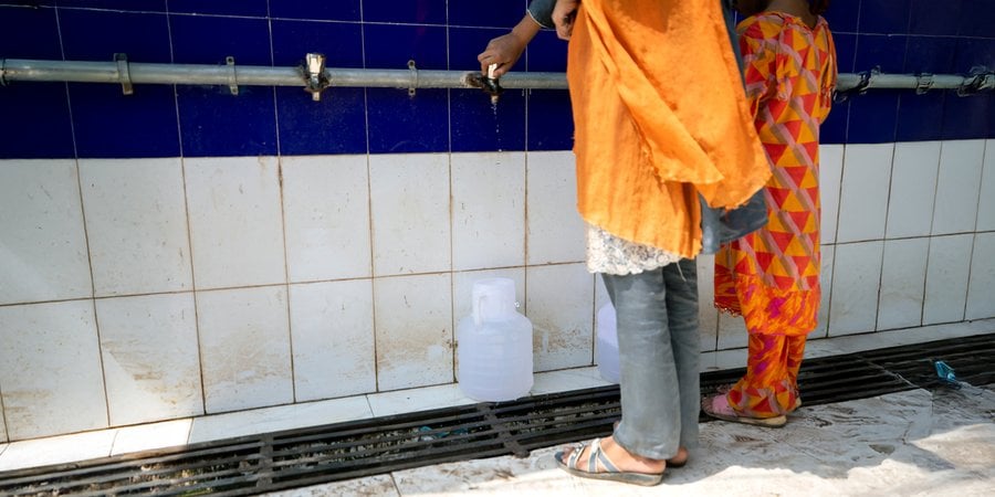 A person stands at a public faucet, filling a bottle