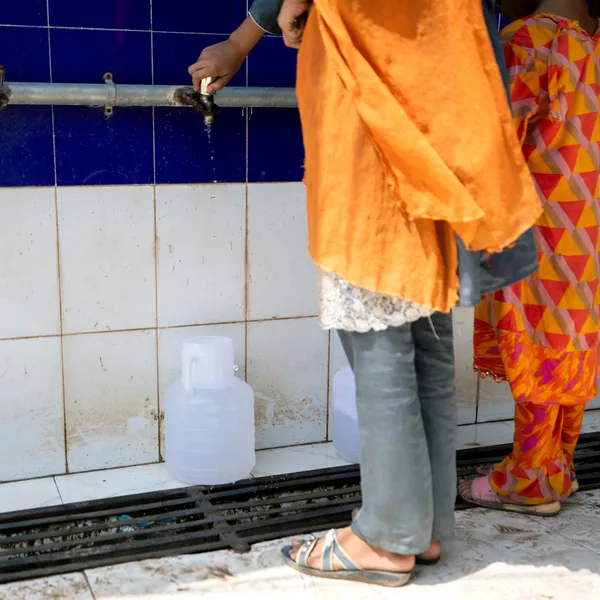A woman collects water at a public faucet