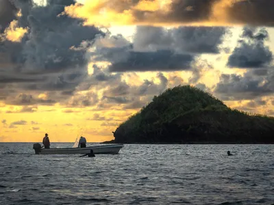 A small boat on the ocean at sunset, an island on the horizon
