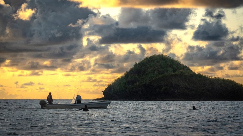 A small boat on the ocean at sunset, an island on the horizon