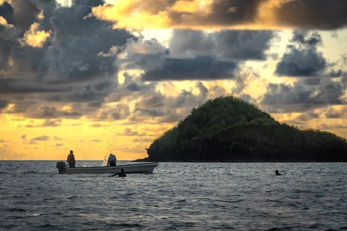 A small boat on the ocean at sunset, an island on the horizon