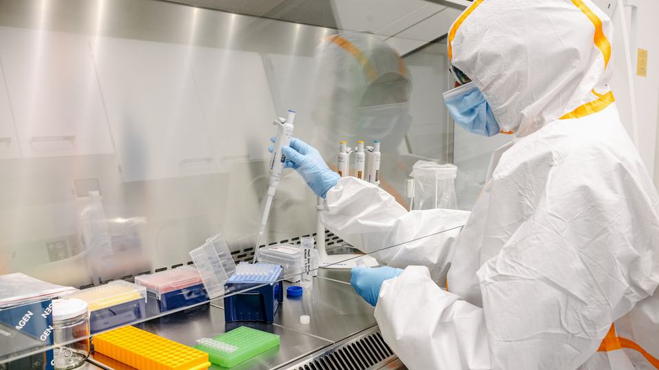 A worker in sterile lab clothing using pipette to transfer sample