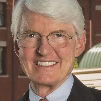 An older white man with gray hair and rectangle metal glasses smiles.